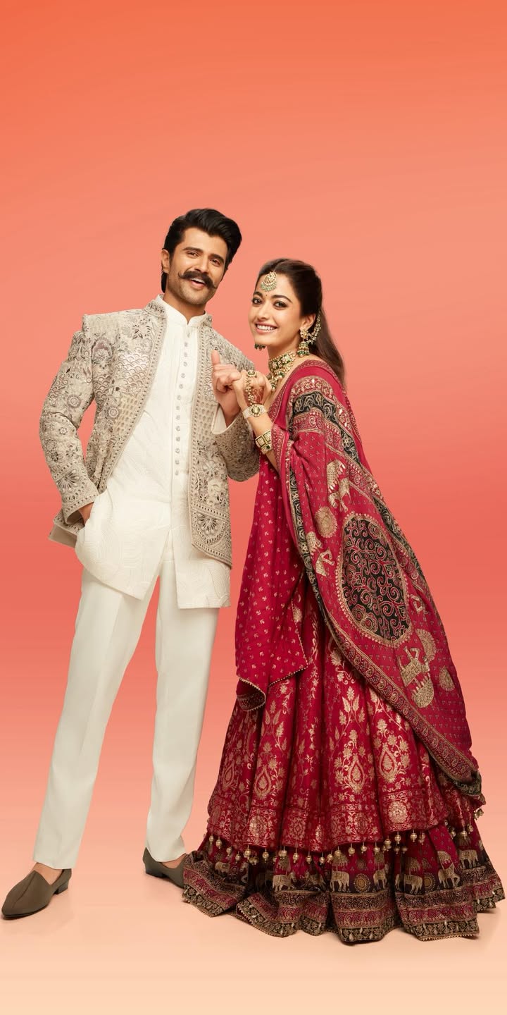 Vijay Deverakonda keeps it classic in a light grey Indo Western from Manyavar, while Rashmika Mandanna stuns in a maroon Moh...