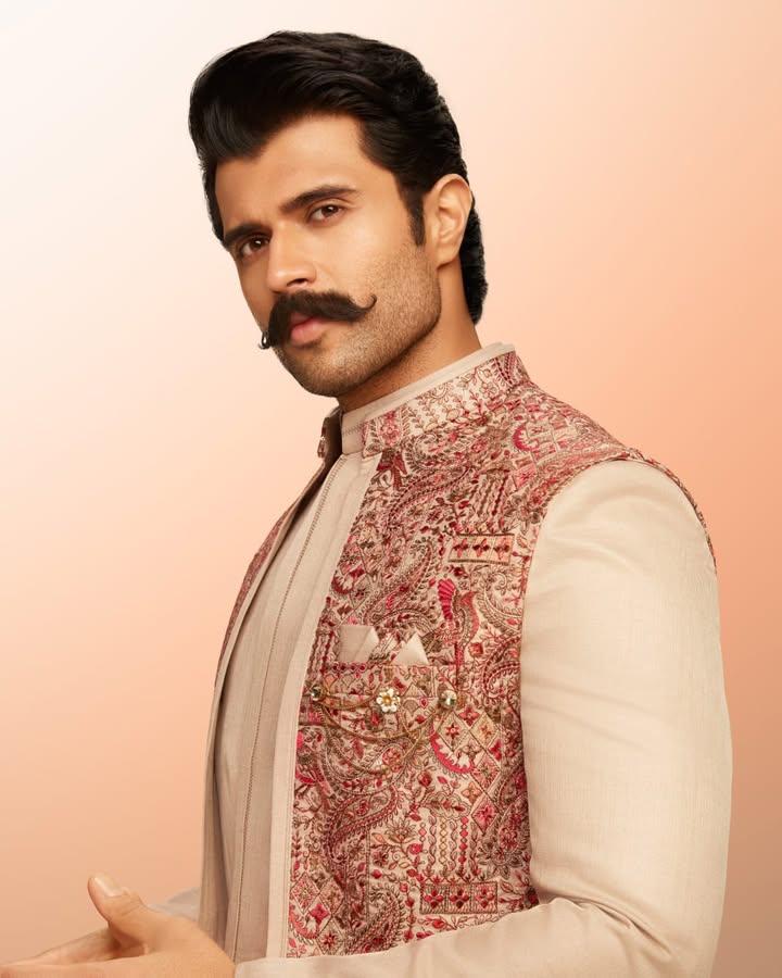 With a structured silhouette and a finely detailed jacket, Vijay Deverakondas Manyavar Indo Western strikes the perfect bala...